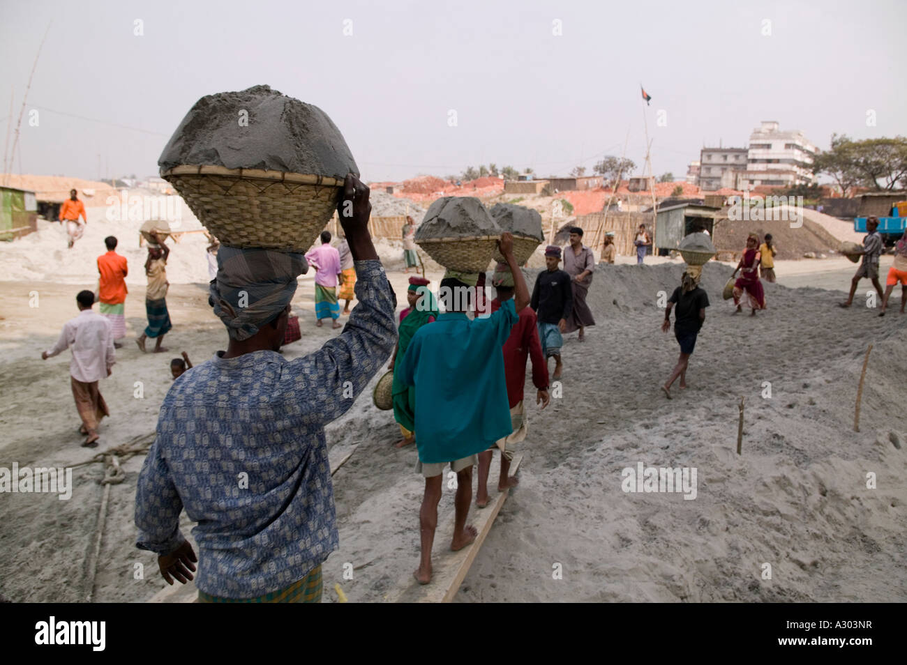 I lavoratori che trasportano pesanti ceste di sabbia sulle loro teste dalla barca alla spiaggia lungo la strada a Savar in Bangladesh Foto Stock