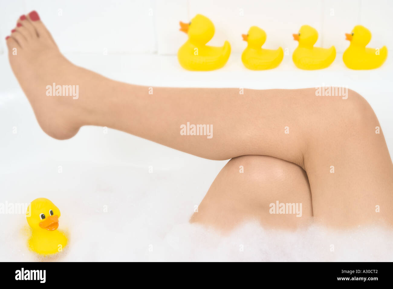 La donna per le gambe in bagno con fila di giallo le papere di gomma lungo il bordo Foto Stock