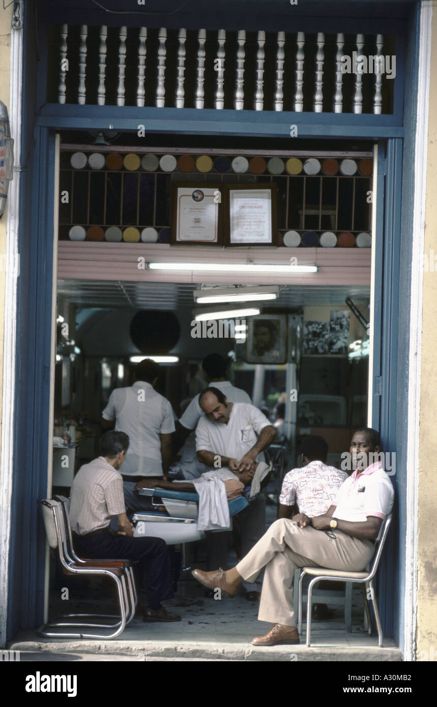 Barbieri sul lavoro a Santiago di Cuba. Gli uomini seduti su sedie in entrata in attesa del loro turno Foto Stock