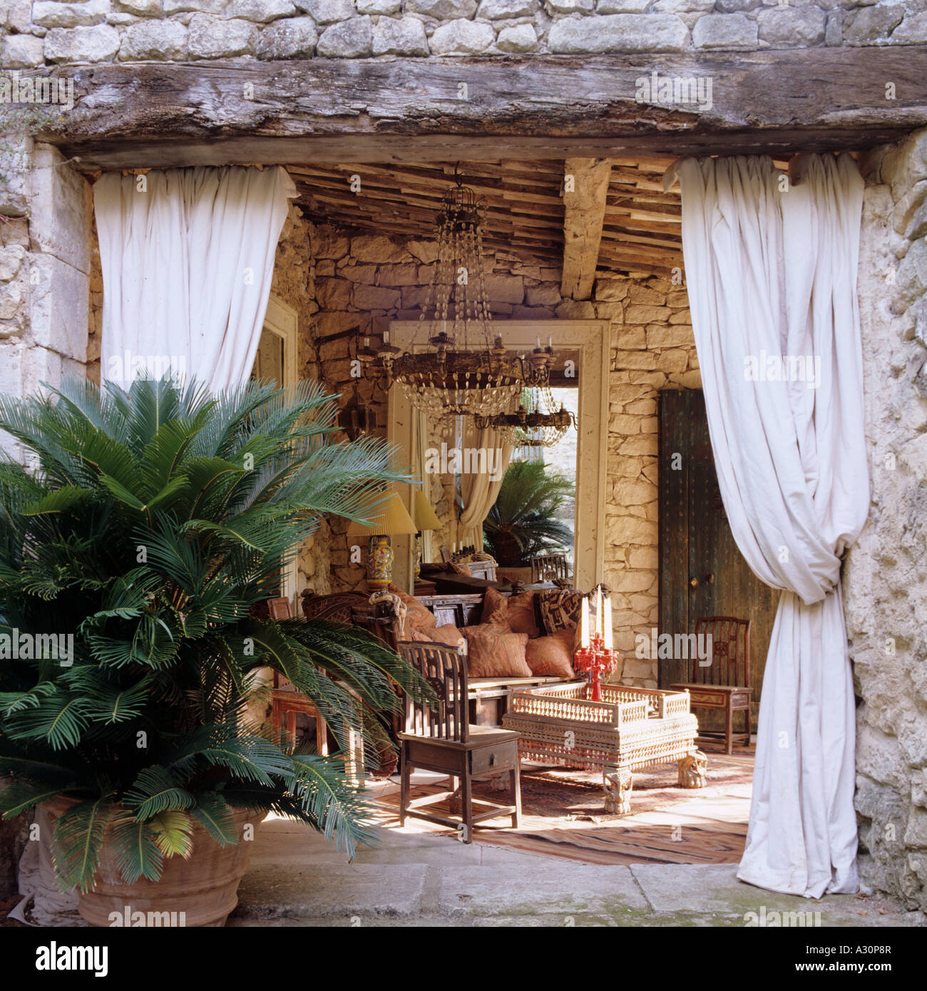 Tavolo in legno e sedie vista attraverso entrata in pietra con tende legato indietro Foto Stock