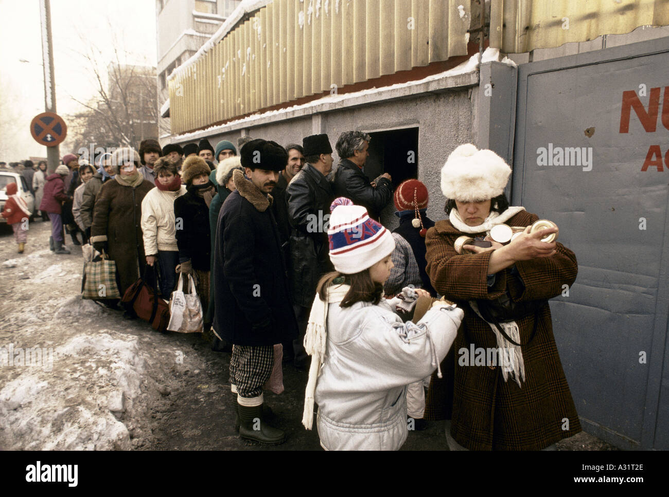La Romania dopo la rivoluzione ragazza madre aiuta con le braccia piene di lattine come altre persone stand accodamento per cibo in strada al di fuori del negozio la costruzione di Bucarest 1990 Foto Stock