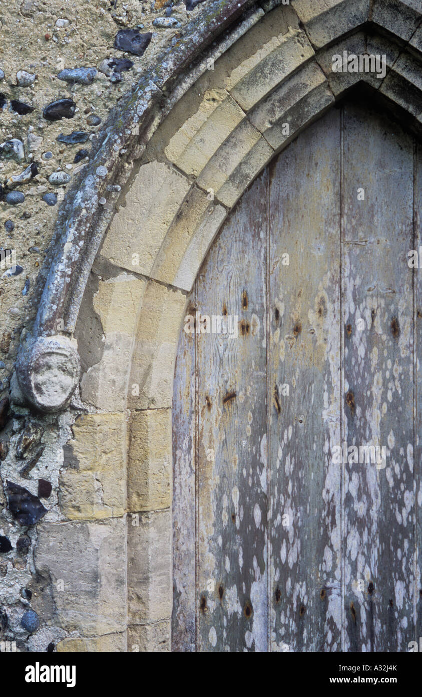 Dettaglio di inizio inglese arcata in pietra con scolpito usurati corbel medievale di testa di donna e porta a spiovente e parete di flint Foto Stock