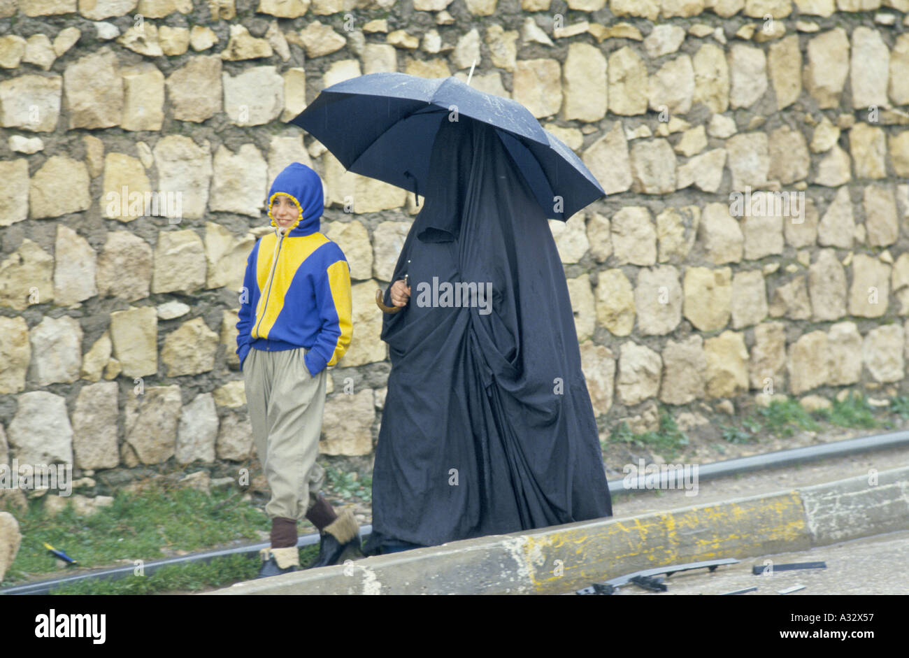 Una Donna vestita di chador tenendo un ombrello a piedi lungo con un ragazzo, Kurdistan Iraq Foto Stock