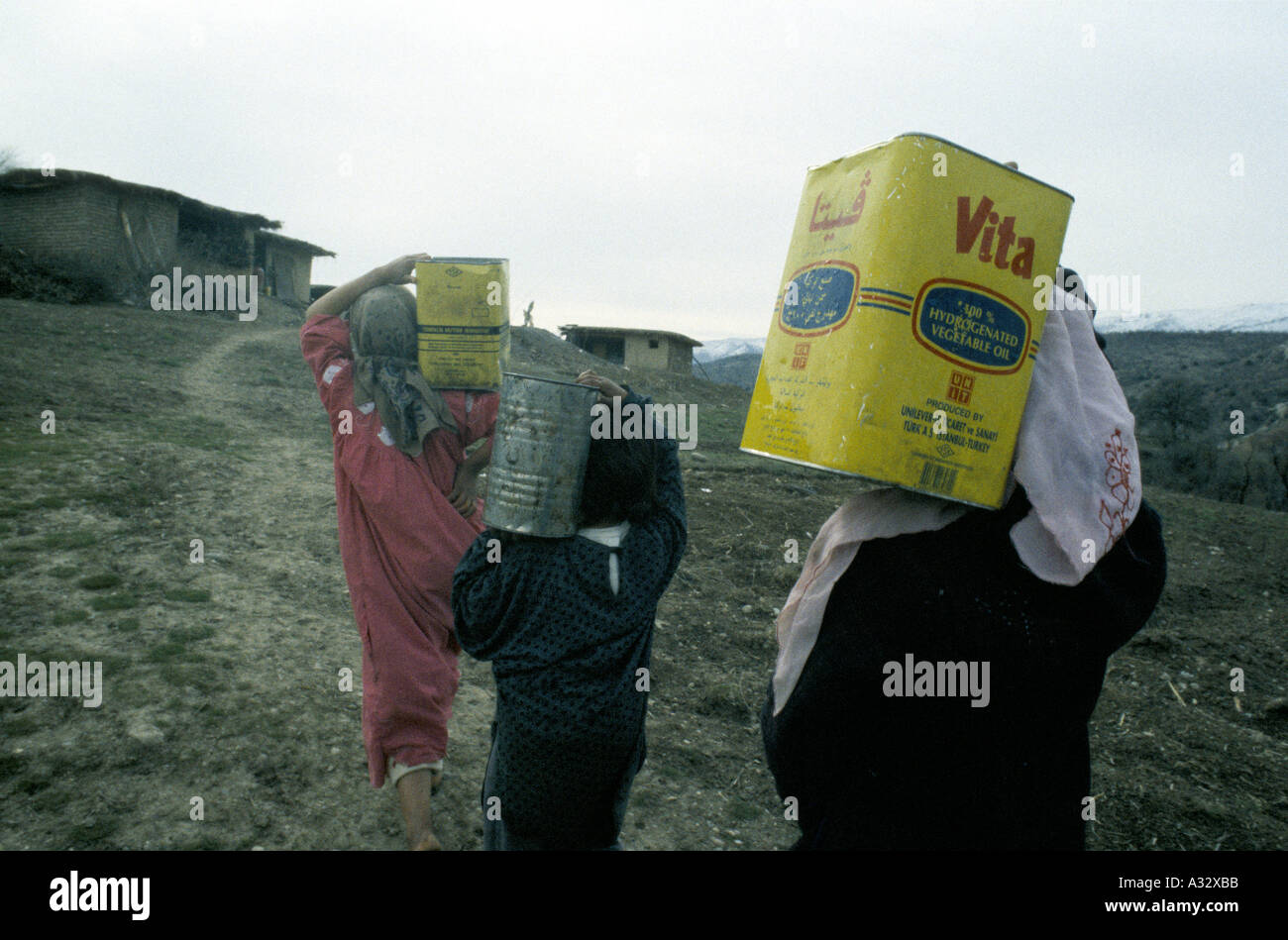 Le donne e i bambini che trasportano petrolio lattine piene di acqua sulle loro spalle su un pendio, Kurdistan, Iraq Foto Stock