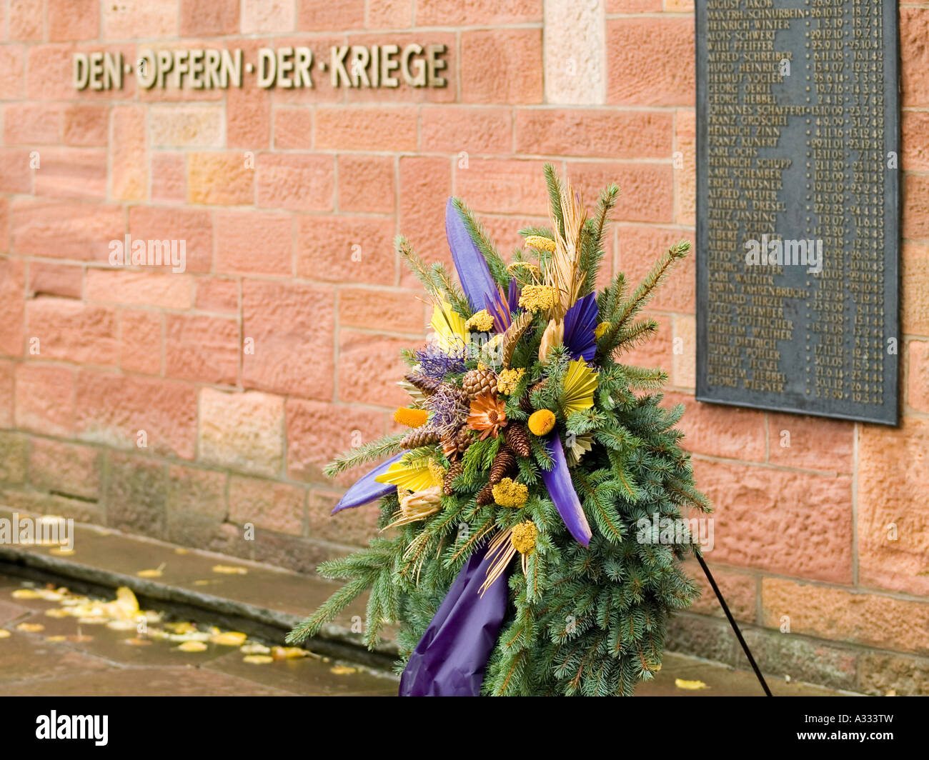 Gridle di fiori nella parte anteriore di una parete con una tabella con i nomi delle vittime del memoriale di guerra per le vittime della guerra Foto Stock