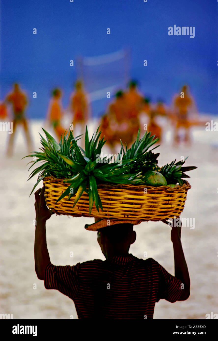 Un fornitore locale porta un cesto di frutta fresca per un gruppo di giocatori di pallavolo sulla spiaggia di Copacabana a Rio de Janeiro in Brasile Foto Stock