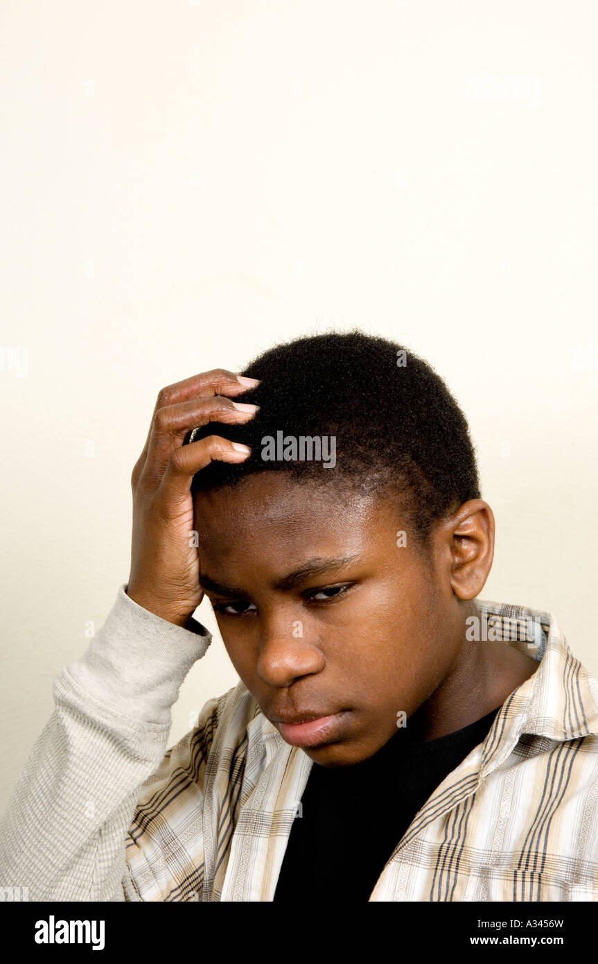 Colpo verticale di un giovane africano American boy mettendo la sua mano sulla sua testa con un espressione triste su sfondo bianco Foto Stock