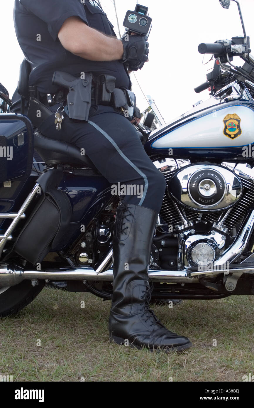 Vista laterale di un poliziotto in uniforme della motocicletta seduto sulla sua moto con un dispositivo di misurazione della velocità nelle sue mani funzionario di polizia astratto Foto Stock