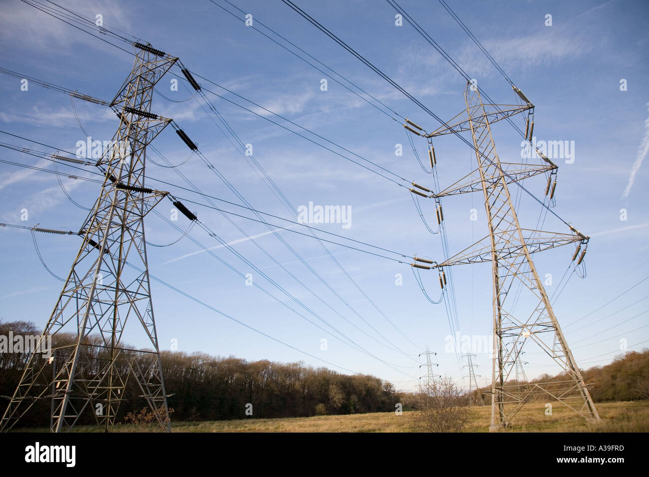 Linee di trasmissione di potenza e tralicci contro un cielo blu con nuvola chiara e terra aperta in primo piano Foto Stock