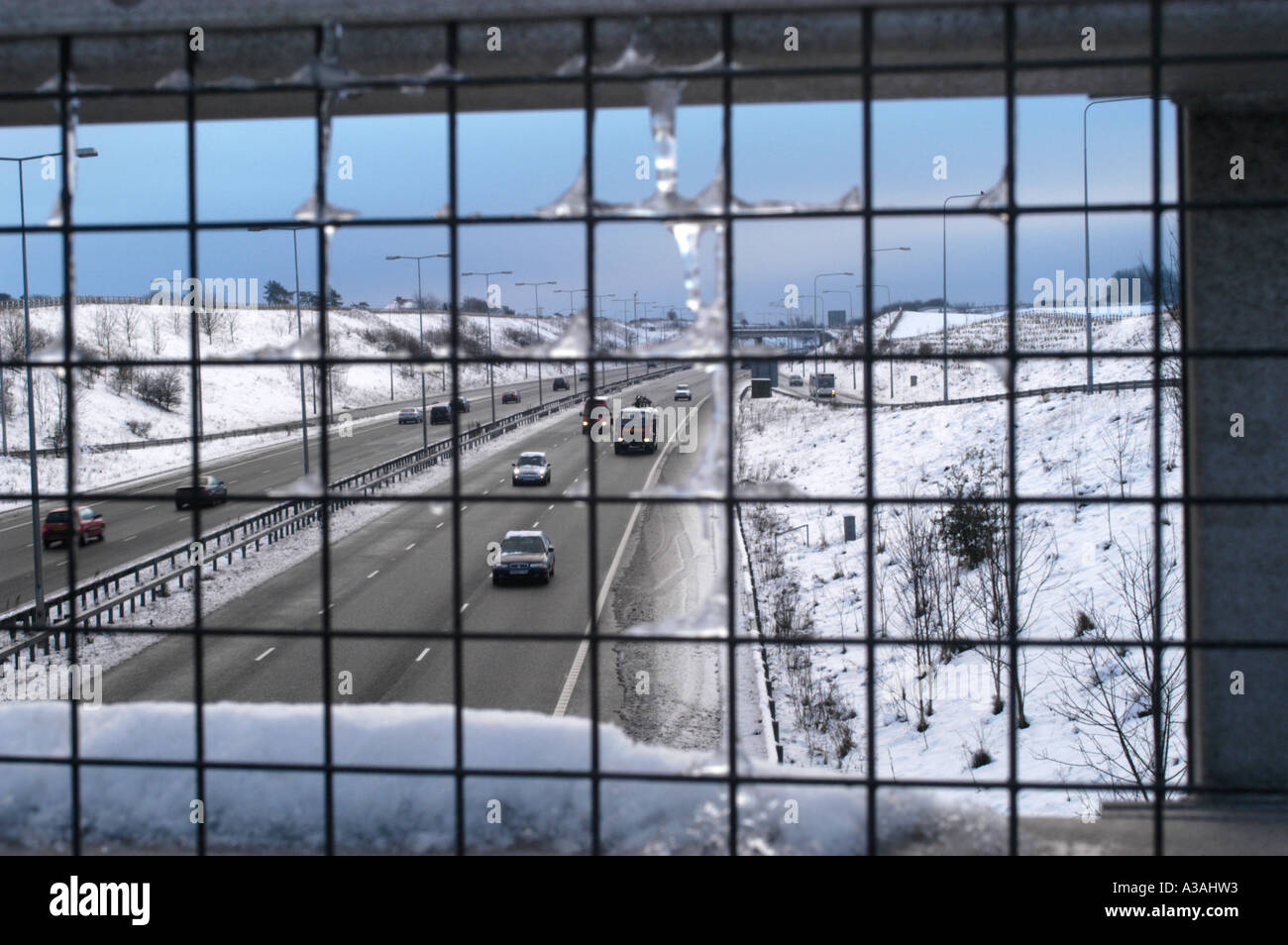 In autostrada in Kent dopo una notte di neve visto attraverso la griglia di recinzione metallica da sopra Foto Stock