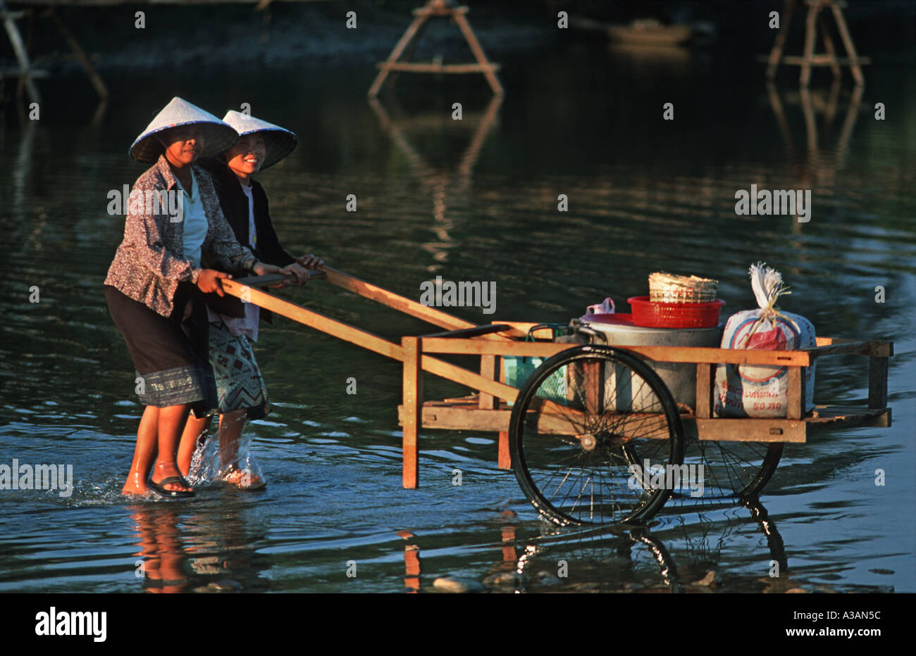 Donne a spingere il carrello di trading attraverso le acque poco profonde di Nam Xong fiume Vang Vieng Laos Foto Stock