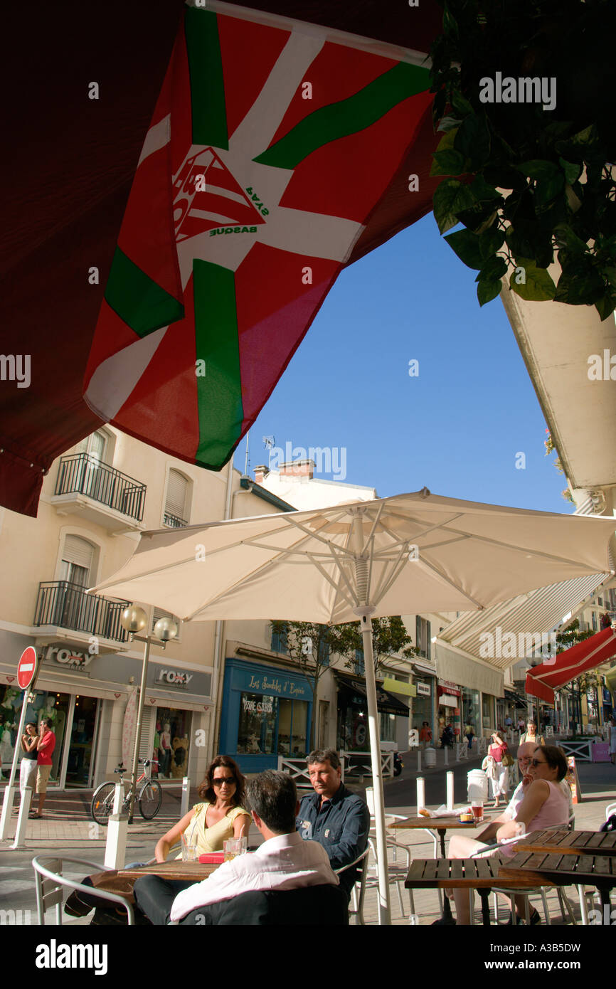 Francia Aquitania Pirenei Atlantique Biarritz gente seduta ai tavoli sul marciapiede sotto gli ombrelloni e una bandiera basca presso un bar Foto Stock