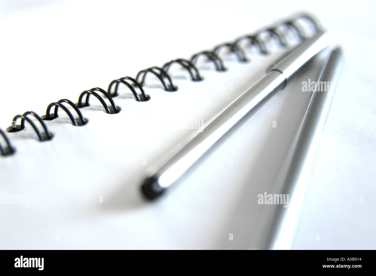 Libro bianco con rilegatura a spirale nera, penna in acciaio inox e matita in argento. Scatto con profondità di campo poco profonda. Foto Stock