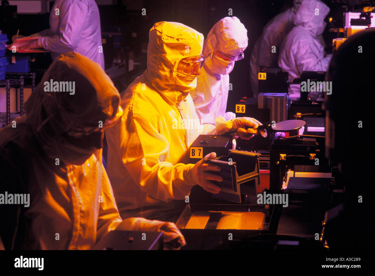 Gruppo di IDT tecnico di laboratorio i lavoratori ispezione di una fetta di silicio in una camera pulita sotto molto Dim lights Foto Stock