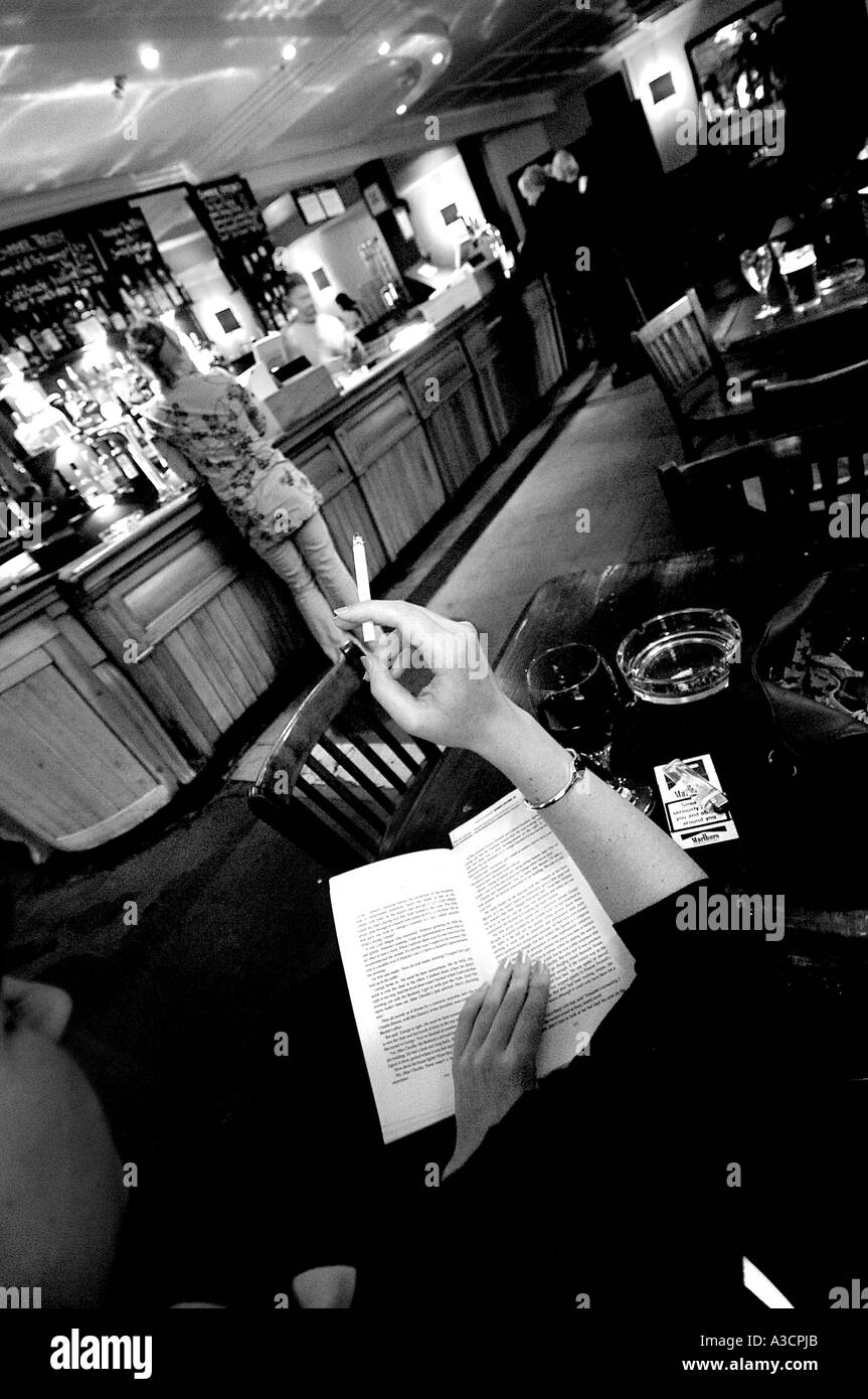 Una signora legge un libro e fuma in Falcon Pub Clapham North London Regno Unito Foto Stock