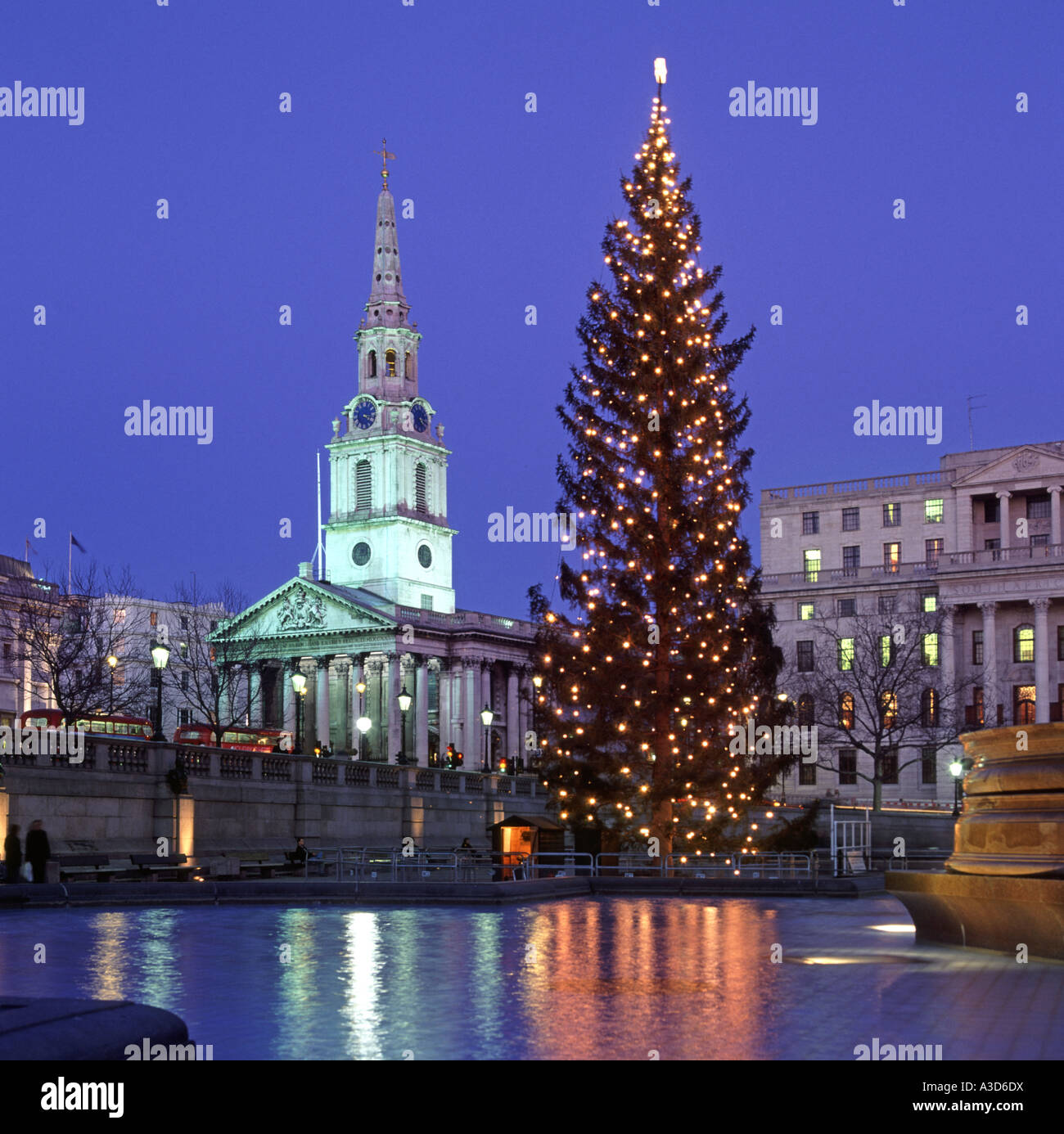 Riflessioni in acqua includono Trafalgar Square Londra Inghilterra REGNO UNITO & albero di Natale luci con proiettori su St Martin nei campi chiesa & guglia Foto Stock