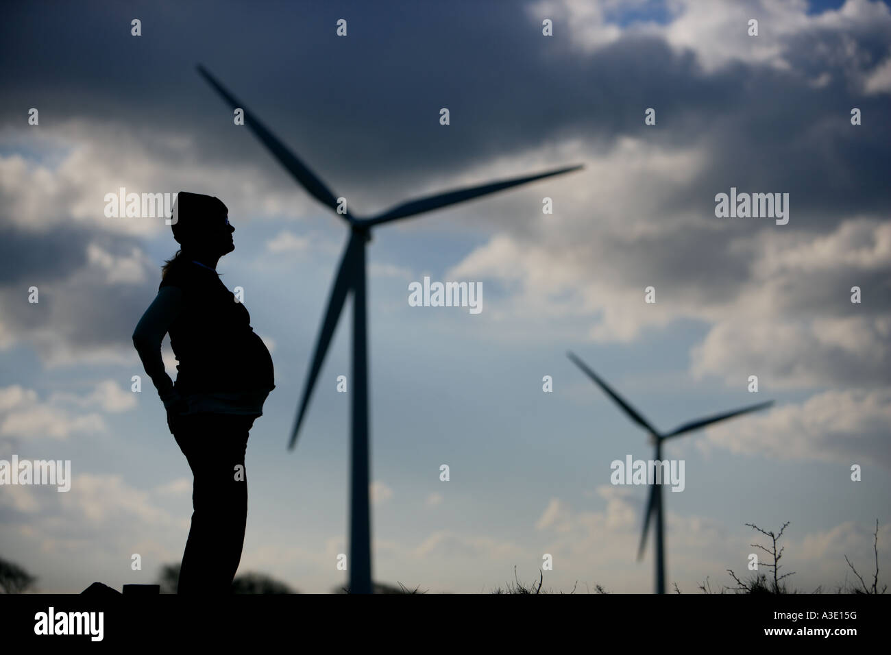 Donne incinte donna incinta guarda ad un futuro più verde in una fattoria eolica, le turbine eoliche in background con drammatica sky Foto Stock
