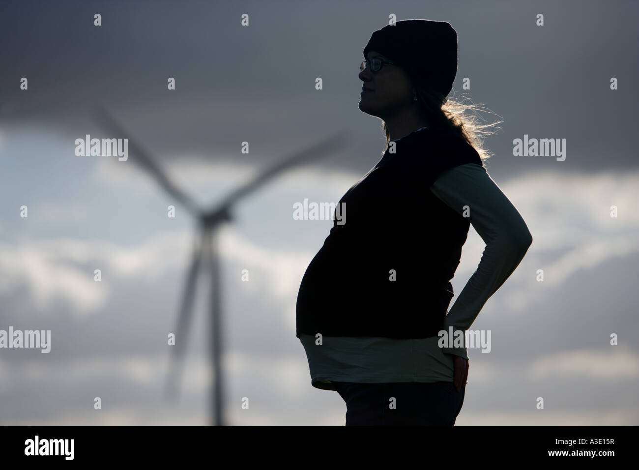 Donne incinte donna incinta guarda ad un futuro più verde in una fattoria eolica, le turbine eoliche in background. in Devon Foto Stock