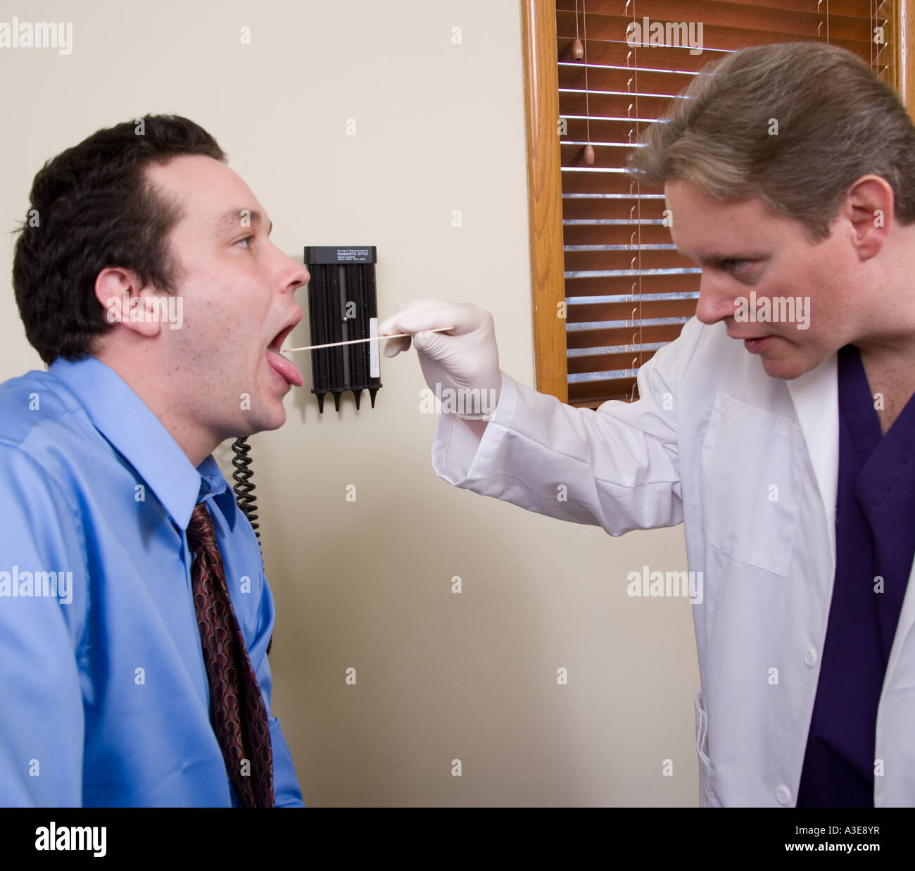 Medico utilizza un abbassa lingua per esaminare l'interno della sua bocca del paziente. Foto Stock