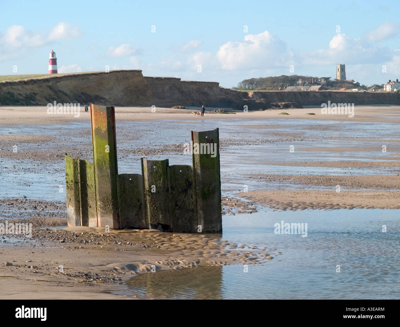 Faro e il campanile di una chiesa con danneggiato le difese del mare con la bassa marea, happisburgh, norfolk, Est Anglia, Regno Unito Foto Stock