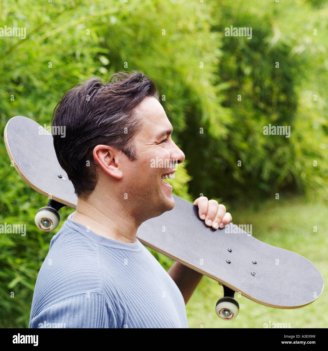 Profilo laterale di un uomo maturo che porta uno skateboard sulla sua spalla e ridendo Foto Stock