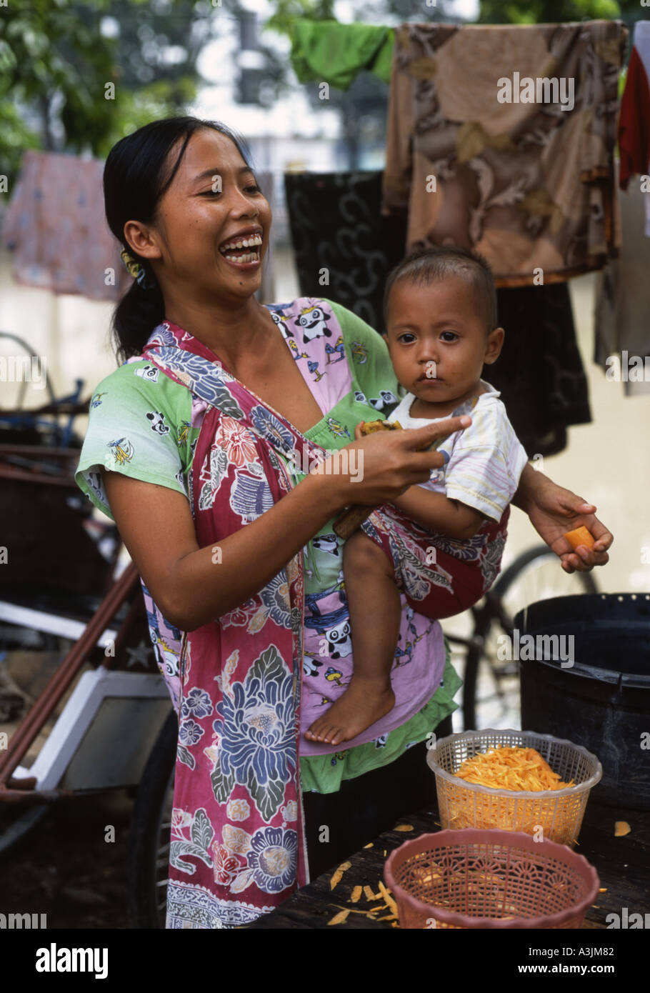 Ridendo madre mentre tiene il suo bambino come si prepara un pasto nella baraccopoli zona di Kalipokor Surabaya East Java Foto Stock