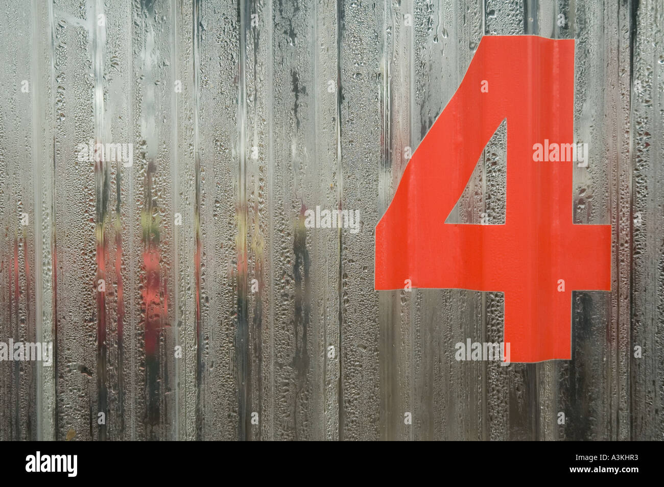 Un gran numero rosso quattro 4 è pubblicato su una serra di plastica porta coperto di condensa Foto Stock
