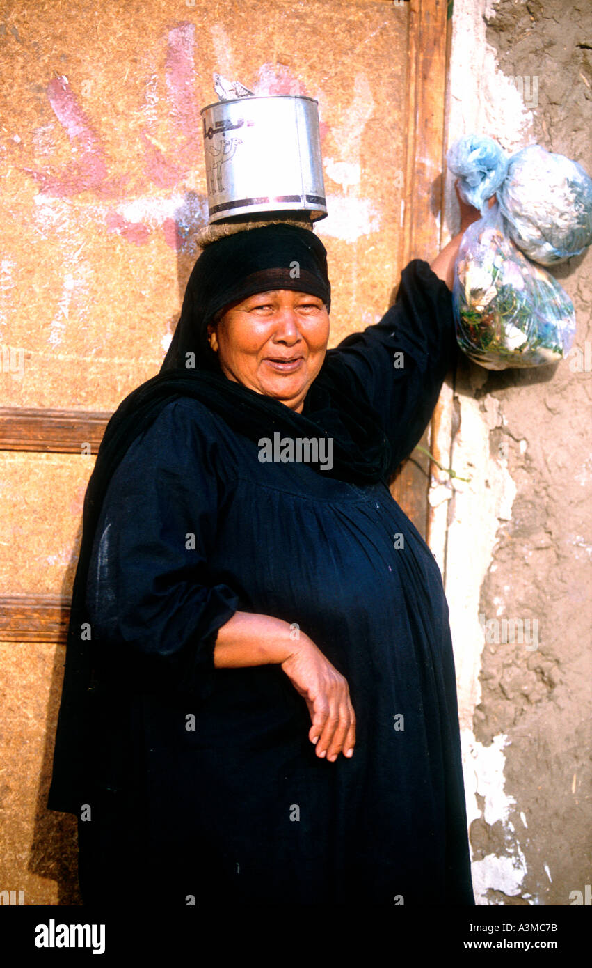 Donna in veste nera porta sacchetti di plastica e può sulla testa Egitto Foto Stock