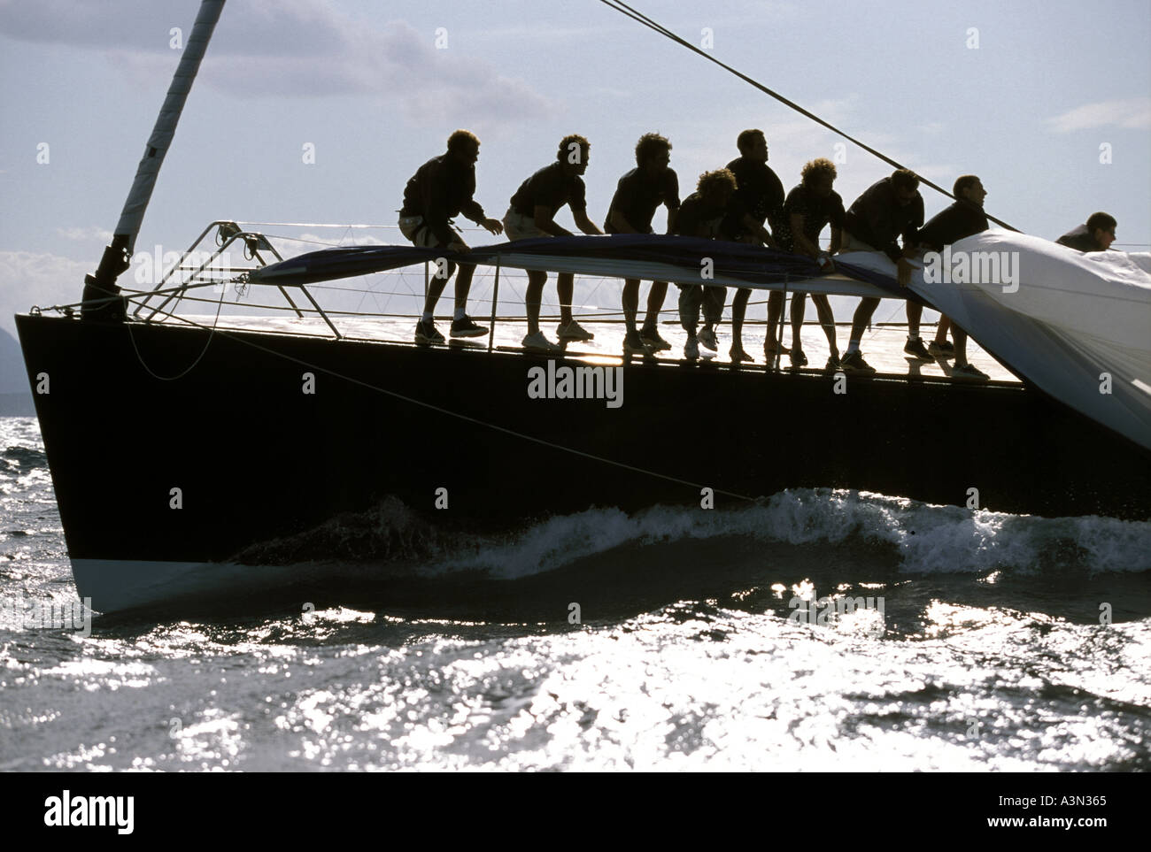 Equipaggio a bordo di una barca da regata di lotta per tirare lo spinnaker a bordo come si trascina in acqua Foto Stock