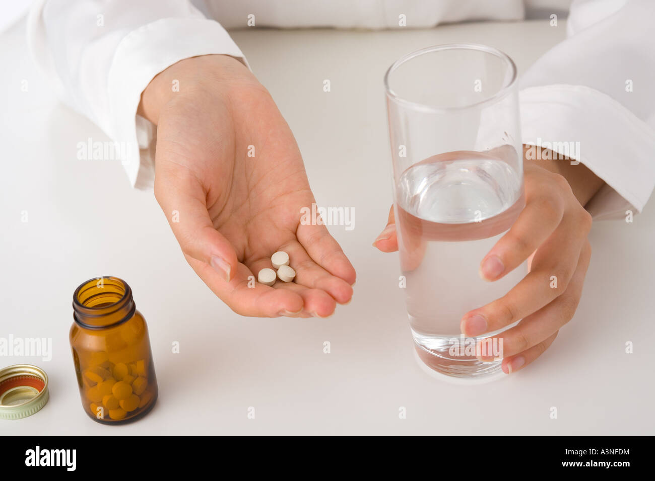Una giovane donna di mano in mano un bicchiere di acqua e pillole Foto Stock