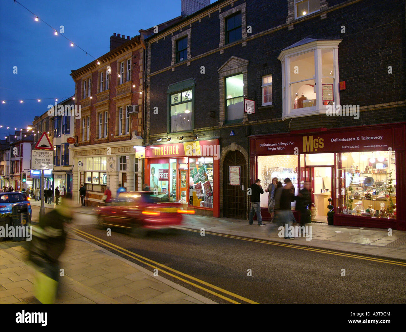 Grande Darkgate street Aberystwyth di notte. La strada principale dello shopping nel Galles occidentale town, negozi illuminati Foto Stock