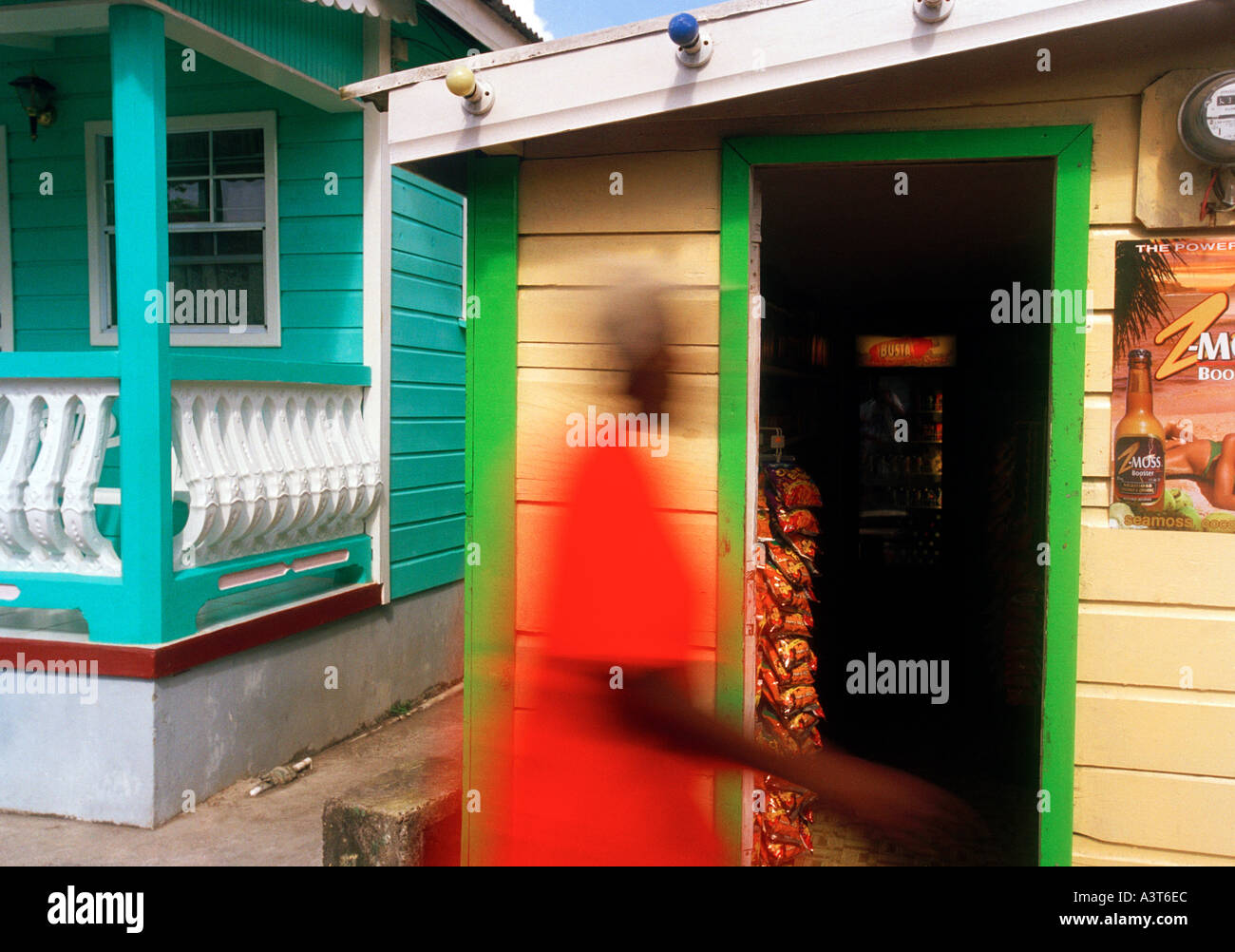 West Indies, caraibi orientali, St Lucia, donna passato a piedi negozi tipici e casa fronti in Anse La Raye movimento sfocato Foto Stock