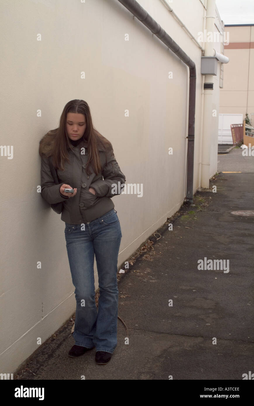 Ragazza adolescente in vicolo appoggiata contro la parete e la lettura di un messaggio di testo sul suo telefono cellulare Foto Stock