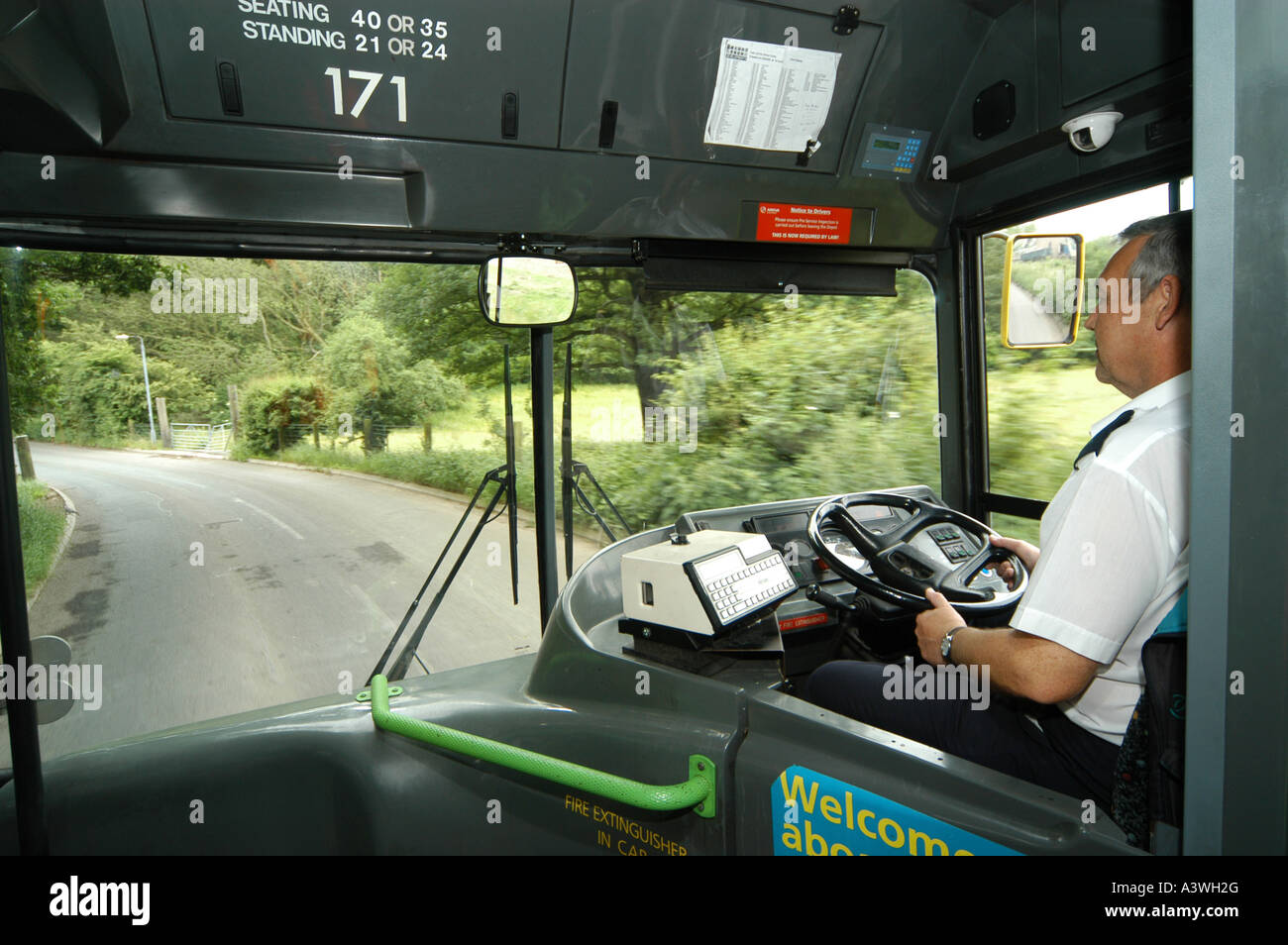 Bus driver di pilotaggio di un bus arriva lungo una strada di campagna nel Regno Unito Foto Stock