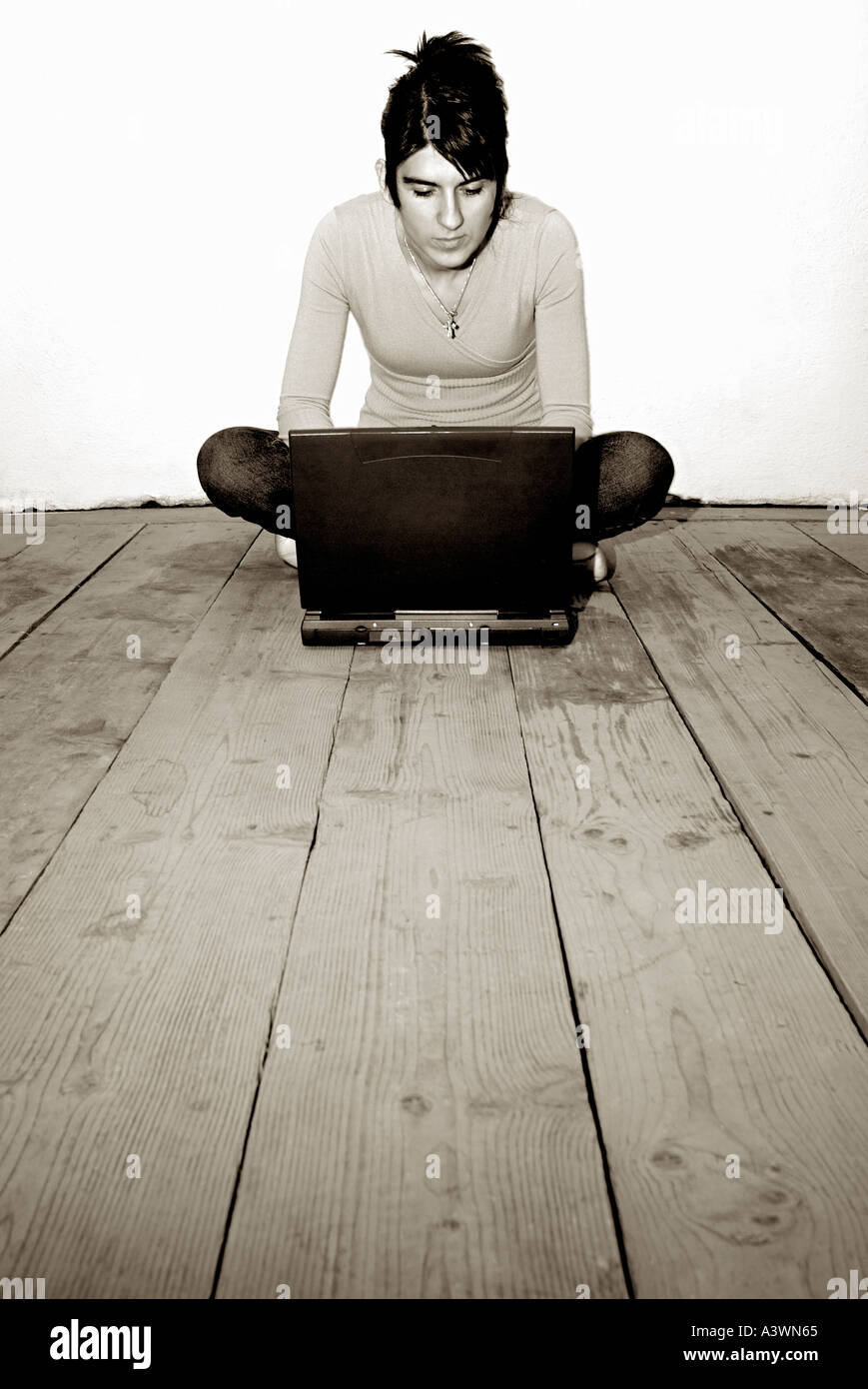 Donna Sat su nude assi di legno utilizzando un computer portatile Foto Stock