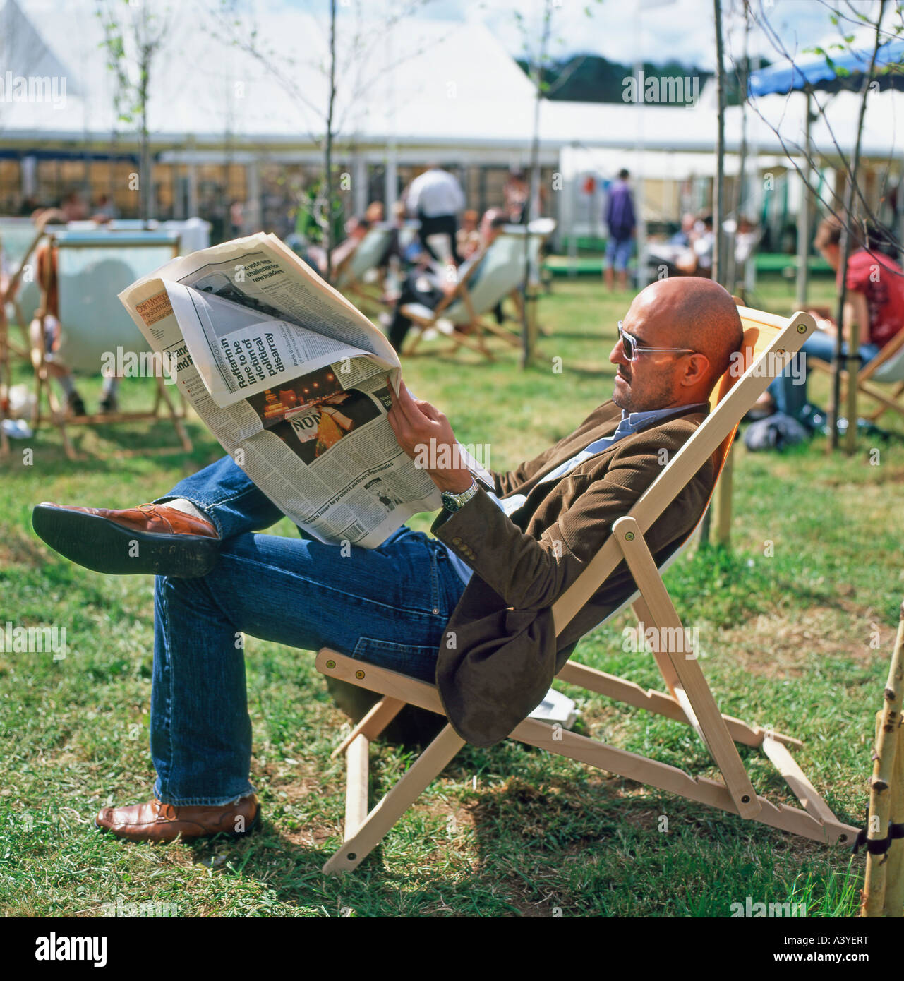 Hari Kunzru rilassante in una sedia a sdraio leggendo un giornale presso il Festival di fieno, Hay-on-Wye, Wales, Regno Unito KATHY DEWITT Foto Stock