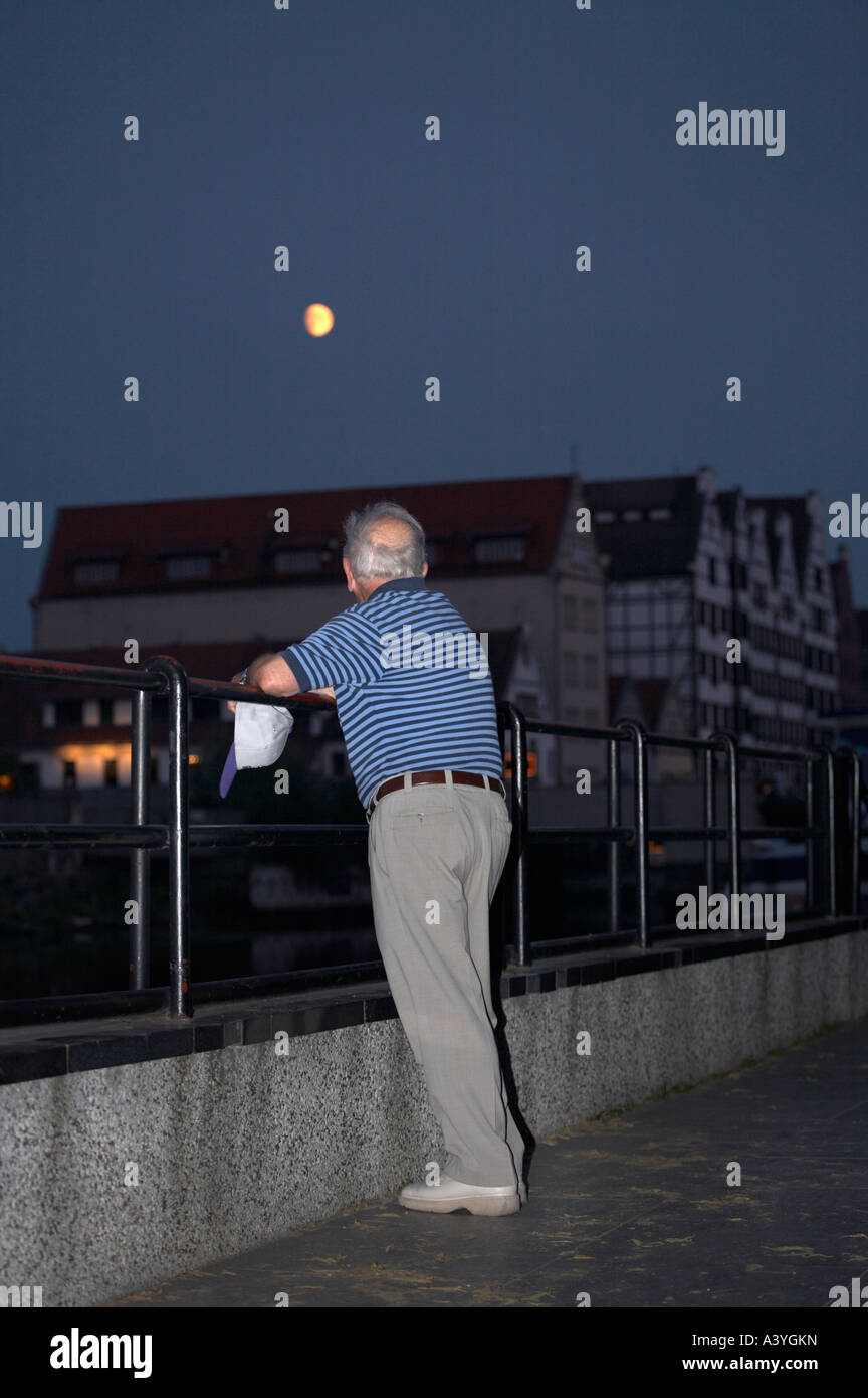 Un uomo maturo è appoggiata contro una ringhiera il peering con la luna. Foto Stock