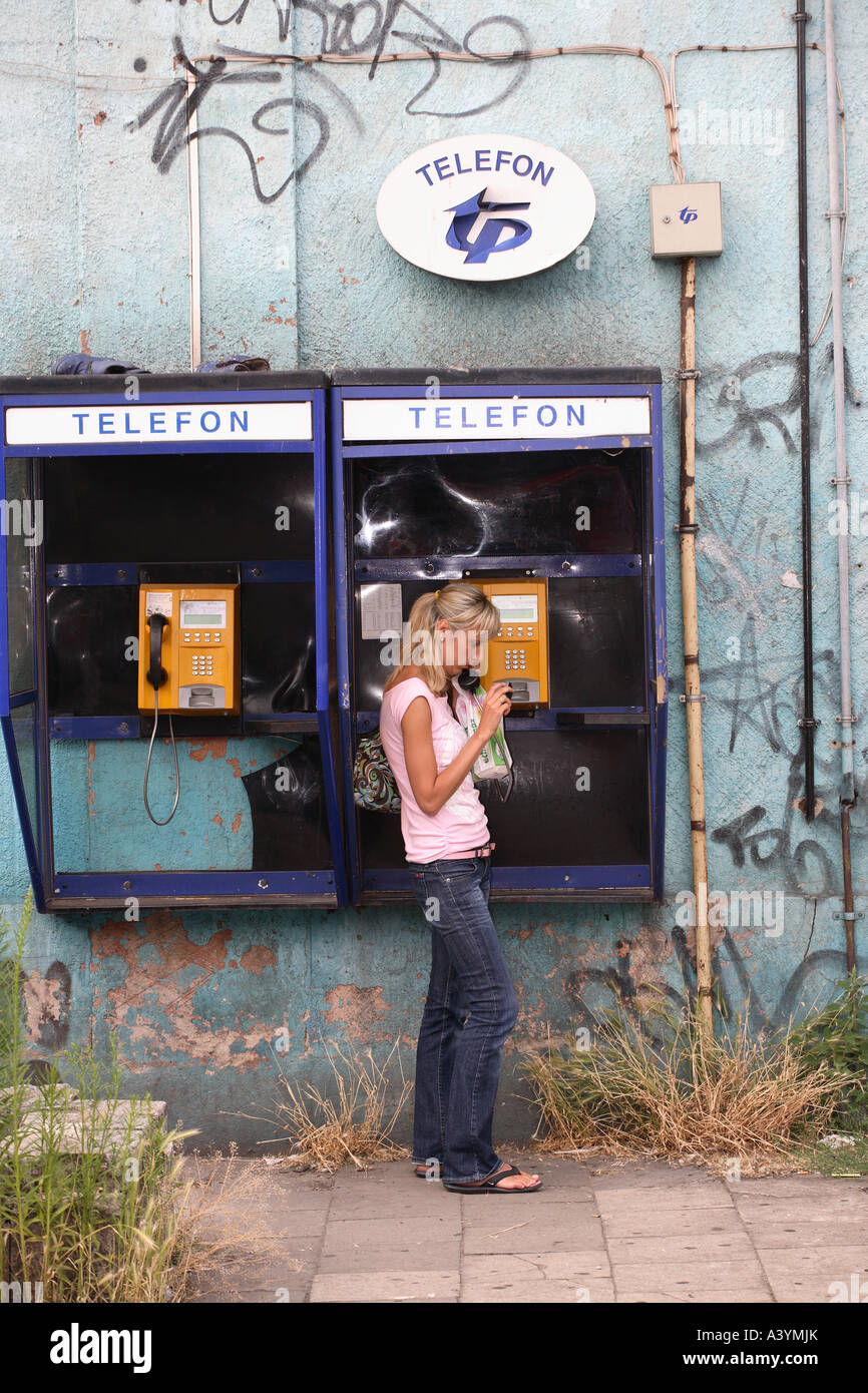 Una giovane donna utilizzando un telefono pubblico in una città interna area coperta in graffit e affetti da trascurare Foto Stock