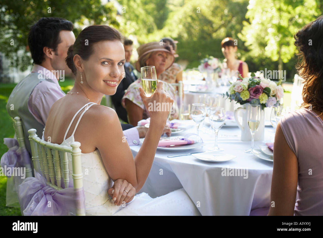 Sposa seduti al tavolo di nozze, tenendo wineglass, sorridente Foto Stock
