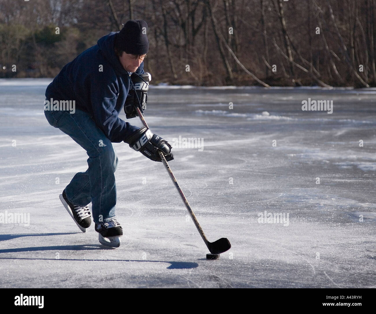 Giovane uomo che gioca hockey su ghiaccio su un laghetto ghiacciato Foto Stock