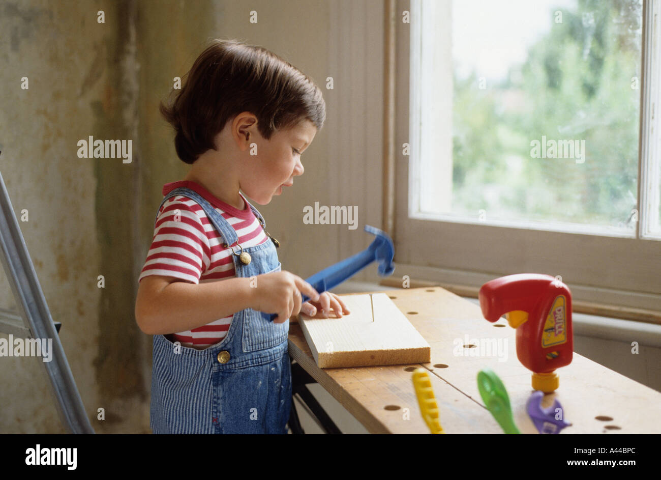 Giovane ragazzo giocando con il giocattolo gli strumenti per il fai da te in una sala decorata Foto Stock