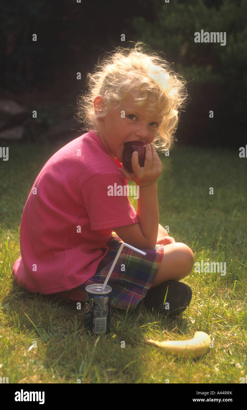 Giovane ragazza seduta su un giardino prato, mangiando un Apple. Foto Stock