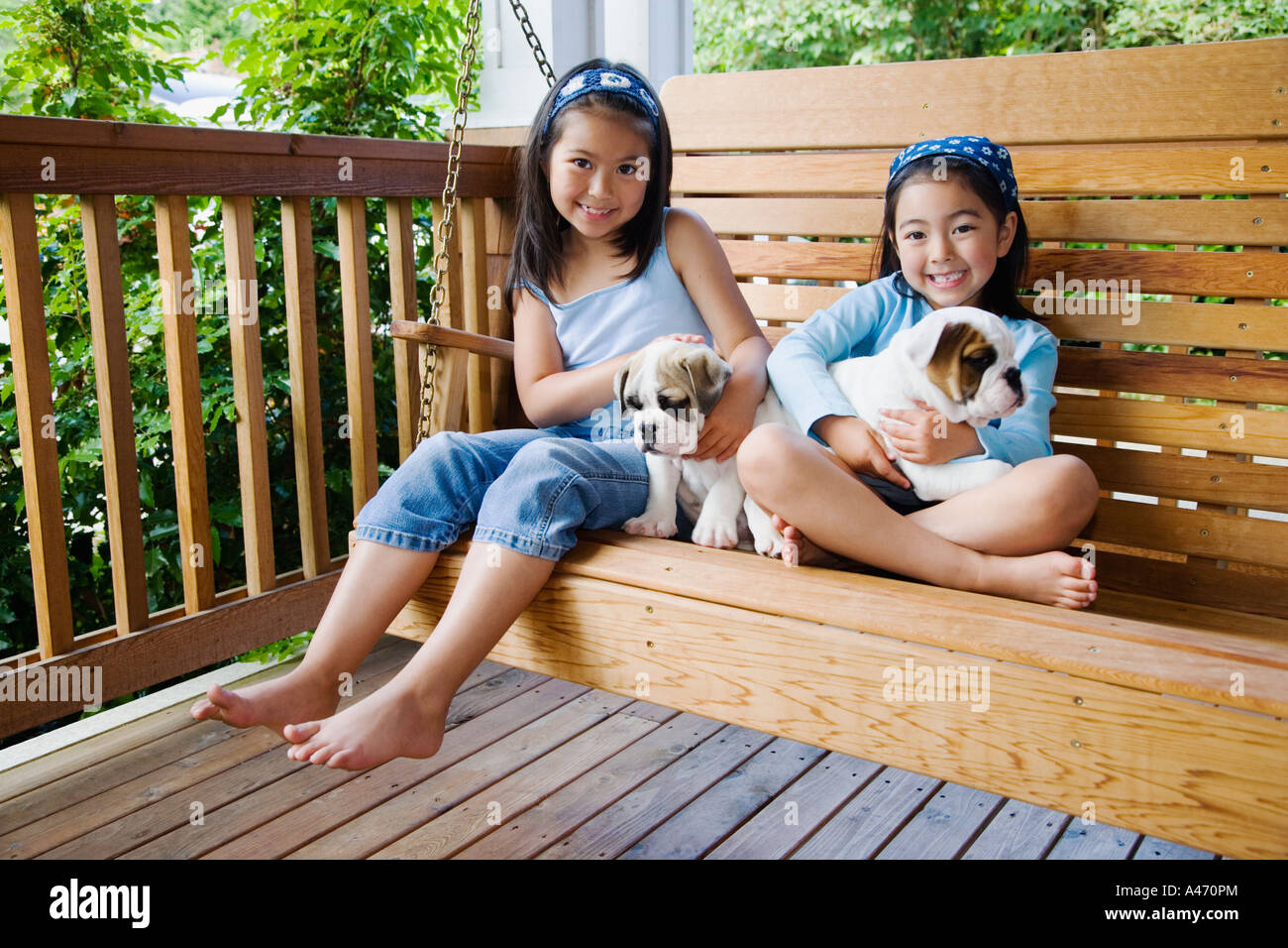 Giovani sorelle asiatiche seduti sulla veranda swing con i cuccioli Foto Stock