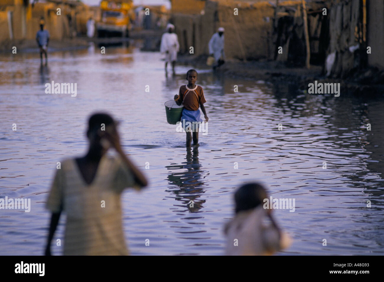 Bambino che porta la benna a piedi attraverso le acque di esondazione dopo il burst del Nilo le sue banche a causa di pioggia pesante sudan 00 06 1988 Foto Stock