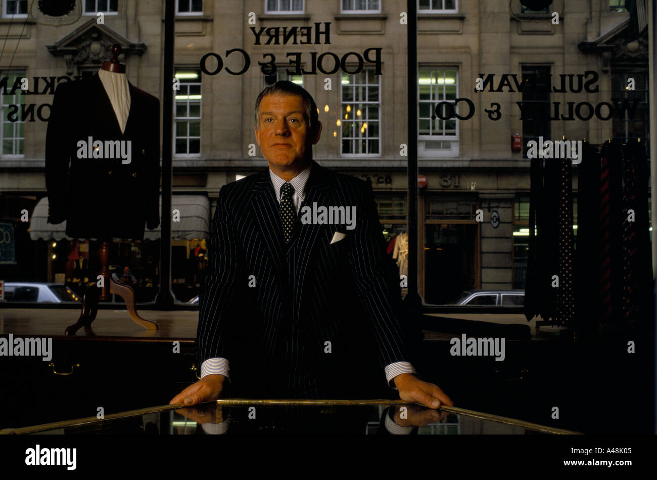 Un sarto in tuta giacca in piedi accanto alla vetrina di un negozio di Saville Row London Foto Stock