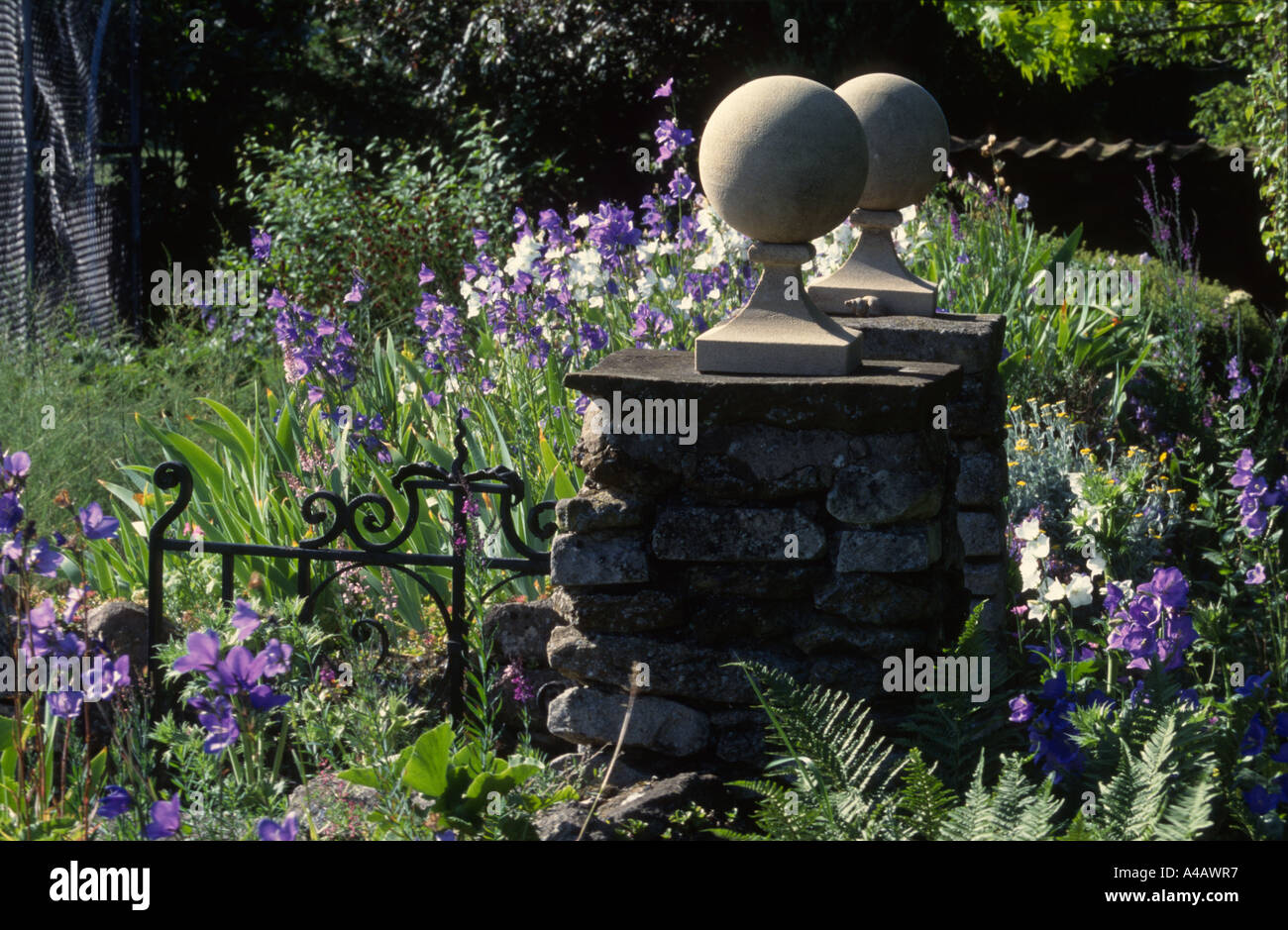 Il nero cancello di ferro con la porta di pietra posti e delphiniums Foto Stock