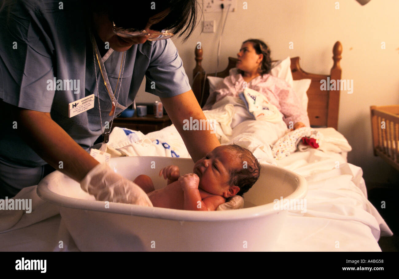 Unità di maternità, Homerton Hospital di Londra, Inghilterra: Un mid-moglie lava un neonato come la madre si rilassa Foto Stock