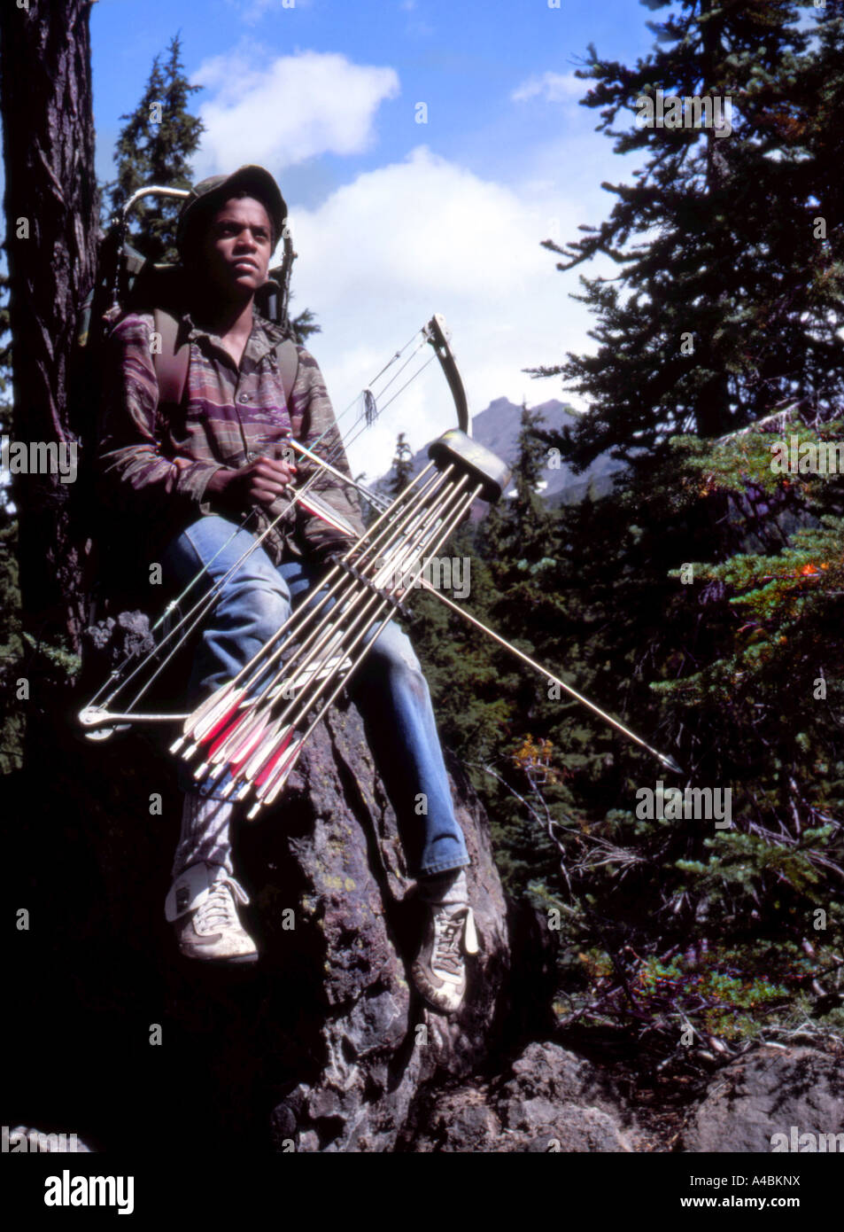 Un giovane ragazzo archer seduto su una roccia, su supporto, tiro con l'arco a caccia di cervi e alci nelle montagne di Oregon Foto Stock