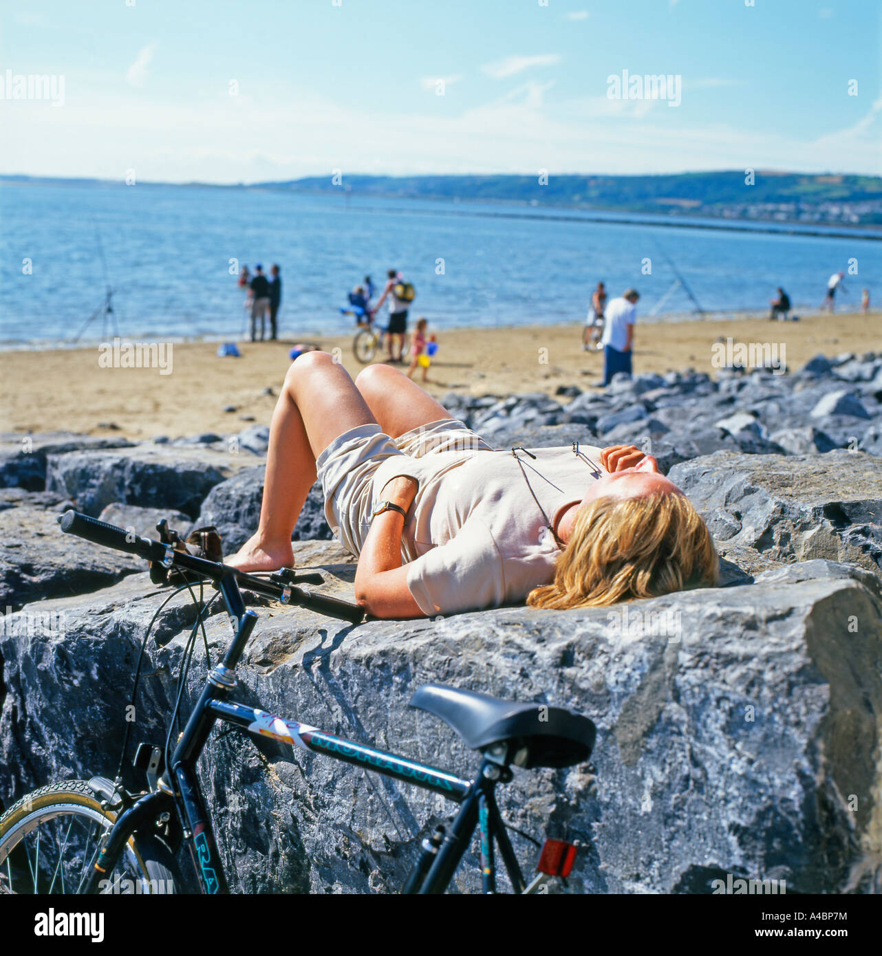 Una donna ciclista femminile che riposa su una roccia nel Millennium Coastal Park vicino Llanelli nel Carmarthenshire Wales Coastal Path UK KATHY DEWITT Foto Stock