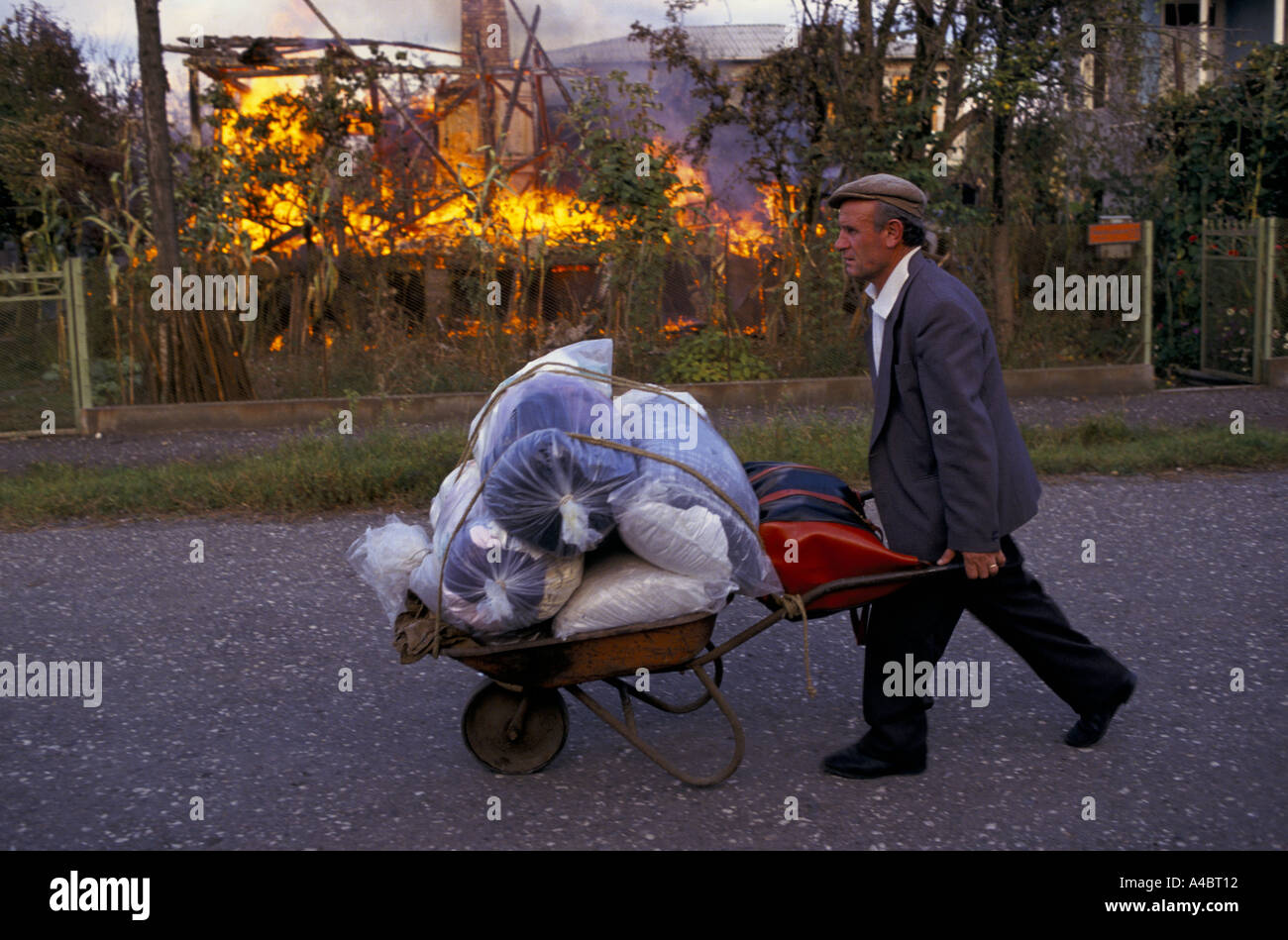 OCHAMCHIRE, GEORGIA, 28 settembre 1993: un uomo spinge i suoi beni in una carriola passato una casa in fiamme come i Georgiani Ochamchire abbandona il giorno dopo la caduta di Sukhumi a Abkhazian le forze separatiste. Foto Stock